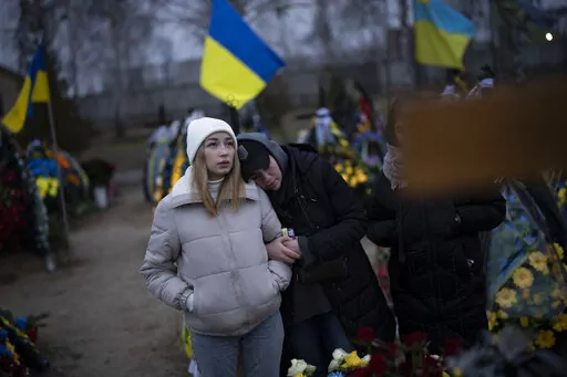 Anastasiia Okhrimenko, left, and Anna Korostenska visit the cemetery together in Bucha, Ukraine, where their partners are buried, Monday, Jan. 23, 2023. As the conflict that killed their loved ones still rages on, Anna, Anastasiia and her brother, Vadym wrestle with a question that all of war-torn Ukraine must grapple with: After loss, what comes next? (AP Photo/Daniel Cole)