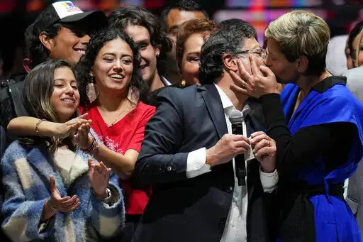 Veronica Alcocer kisses her husband, President elect Gustavo Petro, under the look of their daughters Antonella, left, and Sofia as they celebrate before supporters after he won a runoff presidential election in Bogota, Colombia, Sunday, June 19, 2022. (AP Photo/Fernando Vergara)
