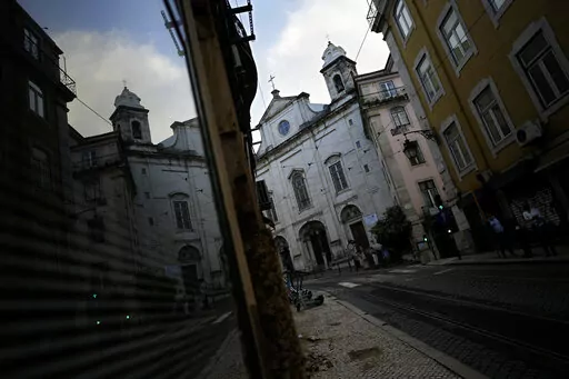 A Catholic church is reflected on a shop window in downtown Lisbon, Tuesday, Oct. 11, 2022. The head of a lay committee looking into historic child sex abuse in the Portuguese Catholic Church said Tuesday in a news conference that the problem has in the past been "widespread" and on some occasions reached "truly endemic" proportions. (AP Photo/Armando Franca)
