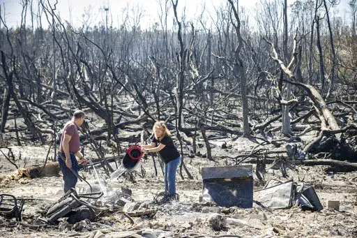 Hector Rivera and Wandi Blanco put water on hotspots behind their home in Panama City, Fla., Saturday, March 5, 2022, following a wildfire that started Friday. The fire destroyed two homes next to them and melted the siding off of their home. (Mike Fender/News Herald via AP)