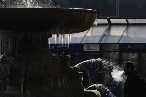 A pedestrian walks past a partially frozen fountain in New York, Tuesday, Jan. 11, 2022. A mass of arctic air swept into the Northeast on Tuesday, bringing bone-chilling sub-zero temperatures and closing schools across the region for the second time in less than a week. (AP Photo/Seth Wenig)