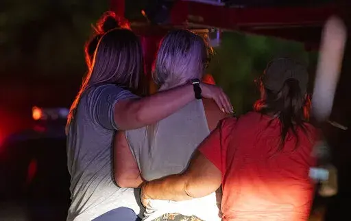 Family and friends embrace each other as Indianapolis Metropolitan Police Department investigators search for a father and three children Tuesday, July 12, 2022, on Bluff Road in Indianapolis. The bodies of a man and three young children were found in an Indianapolis pond amid a search for a father and his kids who had been missing since last week, authorities said Wednesday. (Grace Hollars/The Indianapolis Star via AP)