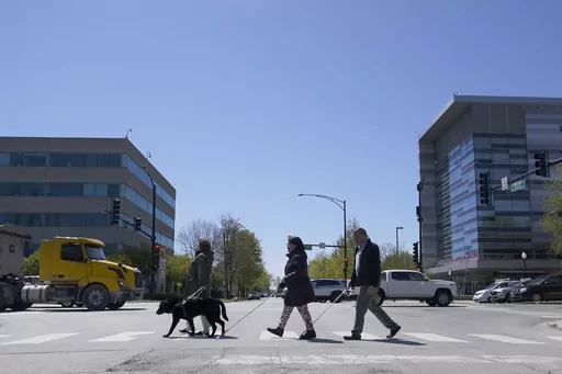 Maureen Reid, left, and her guide dog, Gaston, cross the intersection of Wood Street and Roosevelt Avenue with Sandy Murillo, center, and Geovanni Bahena, relying on an audible signal for the blind, on April 26, 2023, in Chicago. The U.S. Census Bureau wants to change how it asks people about disabilities, and some advocates are complaining that they were not consulted enough on what amounts to a major overhaul in how disabilities would be defined by the federal government. (AP Photo/Charles Rex