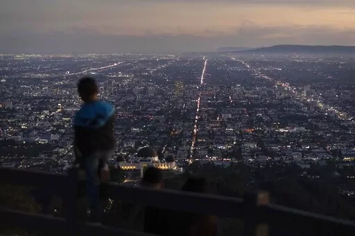 A boy takes in the view of the Los Angeles skyline from the Griffith Park Observatory Trails Peak in Los Angeles, Monday, Nov. 14, 2022. The 8 billionth baby on Earth is about to be born on a planet that is getting hotter. But experts in climate science and population both say the two issues aren't quite as connected as they seem. (AP Photo/Jae C. Hong)