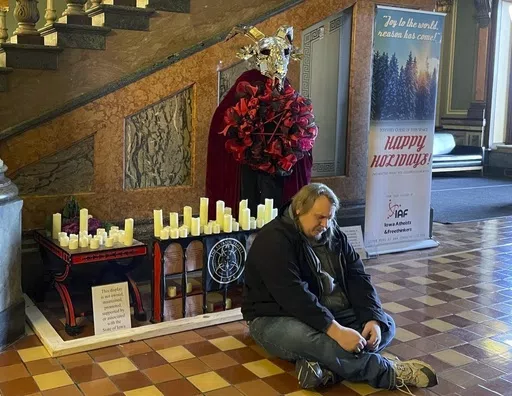 A man prays in Latin in front of a display installed by Satanic Temple Iowa at the Iowa State Capitol in Des Moines, Iowa, on Tuesday, Dec. 12, 2023. A Mississippi man accused of destroying a statue of the pagan idol Baphomet at Iowa's state Capitol pleaded guilty Friday to a reduced charge in return for prosecutors dropping a felony hate crime count. (Caleb McCullough/The Gazette via AP, file)