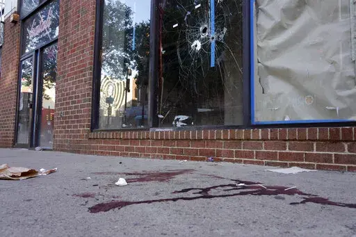 ADDS CONTEXT AND DETAIL THAT THESE BULLET HOLES ARE FROM A PRIOR SHOOTING - Blood is seen at the scene of a fatal overnight shooting on South Street in Philadelphia, Sunday, June 5, 2022, where bullet holes on a storefront window from a prior shooting can also be seen. (AP Photo/Michael Perez)