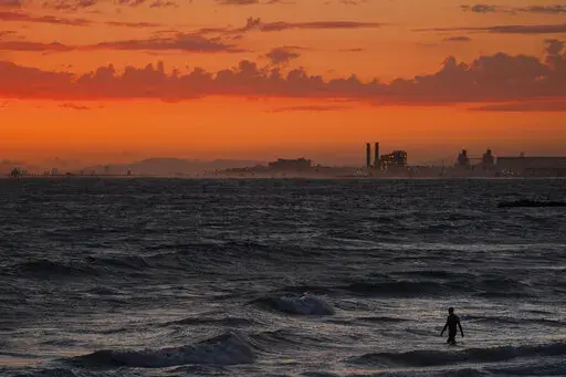 A man wades into the ocean at sunset on June 22, 2021, in Newport Beach, Calif. The National Oceanic and Atmospheric Administration announced Friday, June 3, 2022, that the amount of carbon dioxide in the atmosphere in May averaged 421 parts per million, more than 50% higher than pre-industrial levels. The NOAA said carbon dioxide levels in the air in May have reached a point last known when Earth was 7 degrees hotter, millions of years ago. (AP Photo/Jae C. Hong, File)