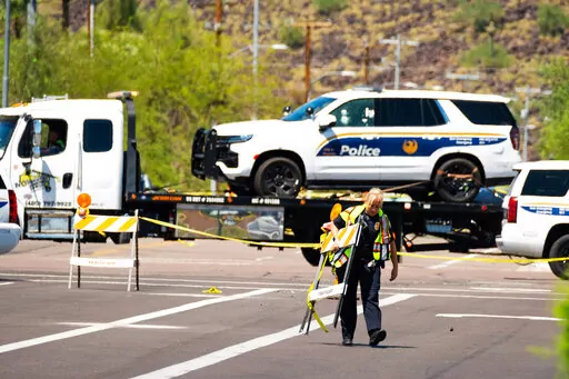 A police officer carries traffic barricades across 27th Avenue near Dear Valley Road, Sunday, Aug. 29, 2022, in Phoenix, as a damaged police vehicle is transported out of the area after a shooting occurred the night before injuring two Phoenix police officers. Americans struggled this week to process not one, but multiple high-profile shootings that unfolded in major cities and smaller towns across the U.S. But behind the stand-out headlines about shooting rampages in Bend, Ore., Phoenix, Detroi