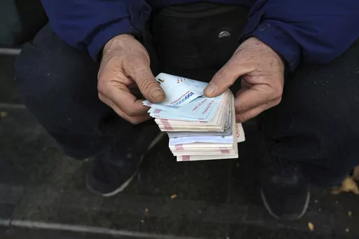 A street money exchanger poses for a photo without showing his face as he counts Iranian banknotes at a commercial district in downtown Tehran, Iran, Friday, Dec. 23, 2022. Iran’s currency fell to a record low on Sunday, plunging to 613,500 to the dollar, as its people celebrated the Persian New Year. (AP Photo/Vahid Salemi, File)