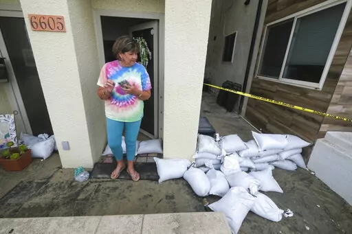 Sue Allen stands next to the sandbags lining at her home after a tropical storm on Saturday, Sept. 10, 2022, in Long Beach, Calif. Southern Californians welcomed cooler temperatures and spotty rain Saturday from a tropical storm veering off the Pacific Coast days after a relentless heat wave nearly overwhelmed the state's electrical grid. (AP Photo/Ringo H.W. Chiu)