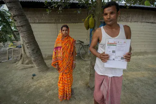 Krishna Biswas, 35, who has not been able to prove his Indian citizenship, shows his Aadhaar card, as his wife Dipali Biswas, 30, stands by outside their house in Murkata village, north eastern Assam state, India, April 15, 2023. Millions of people like Biswas, whose citizenship status is unclear, were born in India to parents who immigrated many decades ago. Nearly 2 million people, or over 5% of Assam's population, could be stripped of their citizenship unless they have documents dating back t