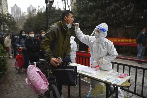 A man holding his bicycle with a school bag on it gets a throat swab during a mass COVID-19 test at a residential compound in Wuhan in central China's Hubei province, Tuesday, Feb. 22, 2022. Wuhan, the first major outbreak of the coronavirus pandemic has reported more than dozen new coronavirus cases this week, prompting the authority to step up precautious measures. (Chinatopix via AP)