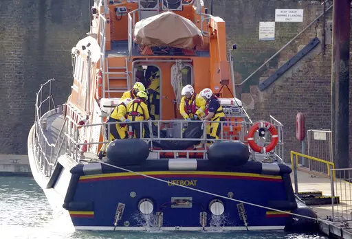 Members of the Dover lifeboat place a body bag on a stretcher after returning to the Port of Dover after a large search and rescue operation launched in the Channel off the coast of Dungeness, in Kent, Wednesday Dec. 14, 2022, following an incident involving a small boat likely to have been carrying migrants. Helicopters and lifeboats have been dispatched to the English Channel off the coast of Kent in southern England to rescue a small boat in distress, authorities said Wednesday. (Gareth Fulle