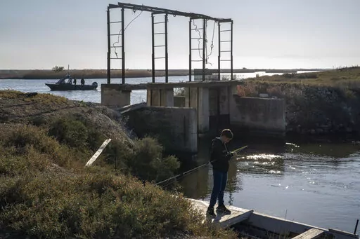 A boy fishes as police border guards on a boat patrol along the Evros River that forms a natural border between Greece and Turkey, on Sunday, Oct. 30, 2022. Greece is planning a major extension of a steel wall along its border with Turkey in 2023, a move that is being applauded by residents in the border area as well as voters more broadly.(AP Photo/Petros Giannakouris)