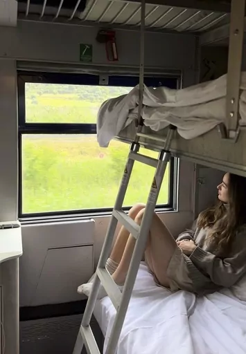 Sarah Marks, of London, looks out at the Italian countryside on TrenItalia's Intercity Notte sleeper train from Palermo to Rome, on June 10, 2023. A growing number of climate-conscious Europeans are giving up flying in favor of long-haul trains. (Sarah Marks via AP)
