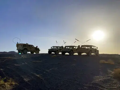 Army vehicles on the ridge, as soldiers from the 2nd Brigade, 1st Cavalry Division, prepare to attack the enemy in the town nearby, during an early morning training exercise at the National Training Center at Fort Irwin, Calif., April 12, 2022. (AP Photo/Lolita C. Baldor)