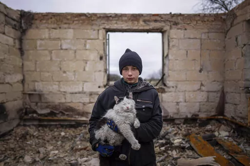 Danyk Rak, 12, holds a cat standing on the debris of his house destroyed by Russian forces' shelling in the outskirts of Chernihiv, Ukraine, Wednesday, April 13, 2022. After shelling Danyk's mother Liudmila Koval had to have her leg amputated and was injured in her abdomen. She is still waiting for proper medical treatment. (AP Photo/Evgeniy Maloletka)