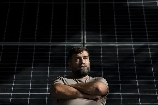 Sebastian Tirintica sits backdropped by solar panels in the RenewAcad training center in Petrosani, southern Romania, Friday, Oct. 11, 2024. (AP Photo/Vadim Ghirda)