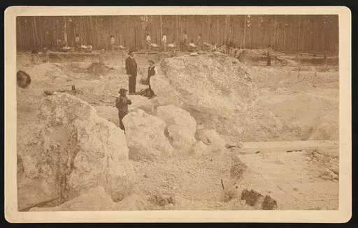 Photograph shows two white men overseeing African American men hammering boulders as others walk with wheelbarrows in a shallow pit phosphate mine, Dunnellon, Florida, 1890. (Library of Congress via AP)