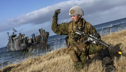 In this image provided by the North Atlantic Treaty Organization, a U.S. marine waves his troops onward after using Dutch landing craft to land near Sandstrand, Norway, March 21, 2022, during the Exercise Cold Response 22. (NATO via AP)