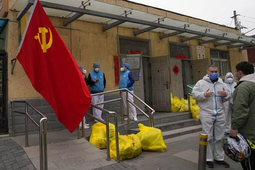 Community workers outside a locked down community chat near a Communist Party flag and trash bags labelled as hazardous waste on Thursday, March 17, 2022, in Beijing. Even as authorities lock down cities in China's worst outbreak in two years, they are looking for an exit ramp from what has been a successful but onerous COVID-19 prevention strategy. (AP Photo/Ng Han Guan)