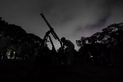 A girl looks at the moon through a telescope in Caracas, Venezuela, on Sunday, May 15, 2022. Six planets will line up in the early morning sky on June 3, 2024 but most won't be visible to the naked eye. A planetary parade happens relatively often when several planets align on the right side of the sun, making them visible across a narrow band of our sky. (AP Photo/Matias Delacroix)