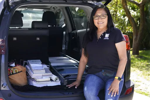 Natalia Ponce De Leon, owner of Custom Window Furnishings, sits on the back of her nine-year-old Toyota RAV4 after visiting with a client, Wednesday, April 13, 2022, in Delray Beach, Fla. Ponce De Leon traded her 2018 Toyota Tacoma for a more efficient car where she estimates will save her hundreds of dollars a month. She is also able to carry all the tools she needs for her business. (AP Photo/Marta Lavandier)