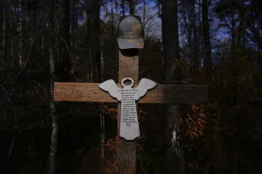 Willie Crayton's hat hangs on a cross bearing the Lord's Prayer and marking the location along Elder Road, Thursday, Dec. 5, 2024, in Dadeville, Ala, where the Alexander City Community Work Center transport van he was riding in crashed in April 2024, killing Crayton and Bruce Clements. (AP Photo/Carolyn Kaster)