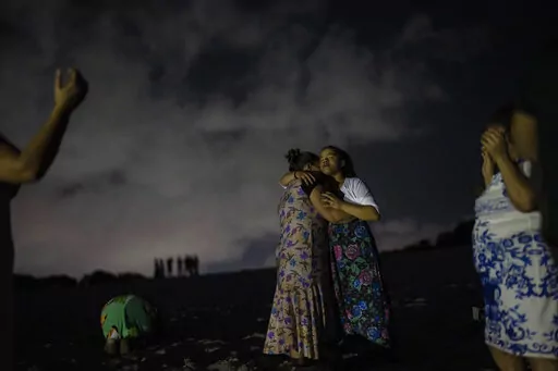 Mag Oliveira embraces her daughter Najla as they pray in an area of the Abaete dune system, on a steep rise of sand evangelicals have come to call the "Holy Mountain", in Salvador, Brazil, late Friday night, Sept. 16, 2022. Evangelicals have been converging on the dunes for some 25 years but especially lately, with thousands now coming each week to sing, pray and enter trancelike states to commune with God.(AP Photo/Rodrigo Abd)