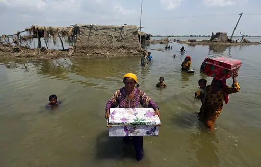 Women carry belongings salvaged from their flooded home after monsoon rains, in the Qambar Shahdadkot district of Sindh Province, of Pakistan, Sept. 6, 2022. From drought to floods and sea level rise, the cost of damage caused by climate change will only get higher as the world warms, sparking concerns from both top officials and activists about how to pay for it. (AP Photo/Fareed Khan, File)