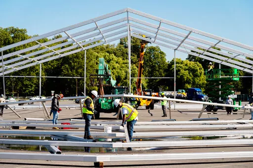 FILE — Workers erect a hangar-sized tent, Sept. 27, 2022, in the parking lot of Orchard Beach, in the Bronx borough of New York, as temporary shelter for thousands of international migrants who have been bused into the Big Apple. New York City's mayor Eric Adams declared a state of emergency on Friday, Oct. 7, over the thousands of migrants being sent from southern border states since the spring, saying the demand being put on the city to provide housing and other assistance is "not sustainabl