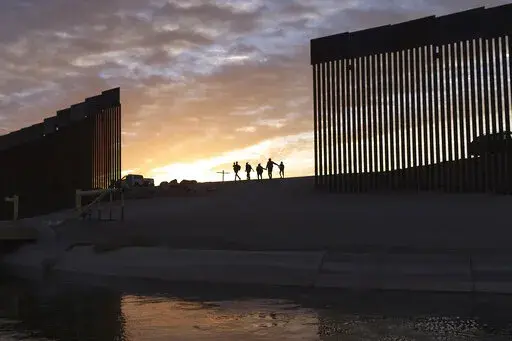 A pair of migrant families from Brazil passes through a gap in the border wall to reach the United States after crossing from Mexico in Yuma, Ariz., to seek asylum on June 10, 2021. The Biden administration may be ending asylum restrictions at the U.S.-Mexico border put in place to stop the spread of COVID-19, but the political and humanitarian challenges for the president may only get worse. (AP Photo/Eugene Garcia, File)
