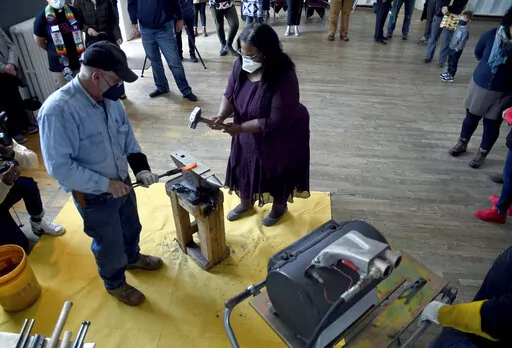 Sharletta Evans, right, whose 3-year-old son, Casson, was killed in a drive-by shooting in 1995, helps Fred Martin, a volunteer blacksmith for the nonprofit group RAWtools, hammer a rifle barrel into a garden tool at a church in Denver, Sunday, Jan. 16, 2022. The Colorado Springs-based group transforms guns into garden tools and draws inspiration from the Bible verse, "They shall beat their swords into plowshares and their spears into pruning hooks." (AP Photo/Thomas Peipert)