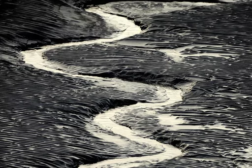 A channel flows through the mud flats along the Seward Highway and Turnagain Arm in Alaska on Oct. 25, 2014. Authorities said, a 20-year-old man from Illinois who was walking Sunday evening, May 21, 2023, on tidal mud flats with friends in an Alaska estuary, got stuck up to his waist in the quicksand-like silt and drowned as the tide came in before frantic rescuers could extract him. (Bob Hallinen/Anchorage Daily News via AP)