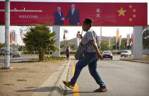 A woman crosses the street near a billboard commemorating the state visit of Chinese President Xi Jinping in Port Moresby, Papua New Guinea, Nov. 15, 2018. China wants 10 small Pacific nations to endorse a sweeping agreement covering everything from security to fisheries in what one leader warns is a “game-changing” bid by Beijing to wrest control of the region. (AP Photo/Mark Schiefelbein, File)