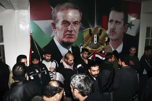 Freed Syrian detainees gather in front of posters showing Syrian President Bashar Assad, right, and his father Hafez Assad after they were released from Adra Prison on the north-east outskirts of Damascus, Syria, on Jan. 15, 2013. A former Syrian military official who oversaw the prison where human rights officials say torture and abuse took place has been arrested in Los Angeles on suspicion of immigration fraud. (AP Photo/Bassem Tellawi, File)