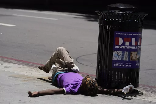 A homeless person lies on the sidewalk while holding a water bottle, Sunday, July 2, 2023, in downtown Los Angeles. Excessive heat warnings remain in place in many areas across the U.S. and are expected to last at least through Monday. (AP Photo/Damian Dovarganes)
