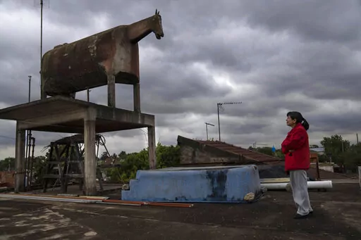 Liliana Gutiérrez looks at the horse-shaped water tank built by her father in the San Jorge neighborhood of Florencio Varela, Argentina, Monday, Oct. 26, 2022. Nostalgia led Gervasio Gutiérrez, a peasant turned bricklayer from the distant province of Jujuy, to build the tank on the terrace of his daughter's house. Before the existence of GPS trackers, the horse-shaped water tank that many confused with a cow, was often used as a reference point for travelers. (AP Photo/Rodrigo Abd)