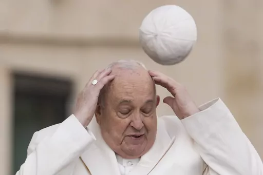 Pope Francis tries to catch his cap as wind blew it away while arriving for his weekly general audience in the St. Peter's Square at the Vatican, Wednesday, March 13, 2024. (AP Photo/Andrew Medichini, File)