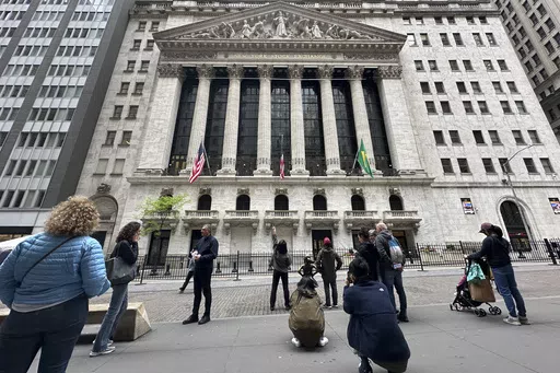Tourists gather near the New York Stock Exchange on May 16, 2024, in New York. Shares retreated in Europe and Asia on Friday, May 24, 2024, after unexpectedly strong reports on the U.S. economy raised the possibility that interest rates may stay painfully high. (AP Photo/Peter Morgan, File)