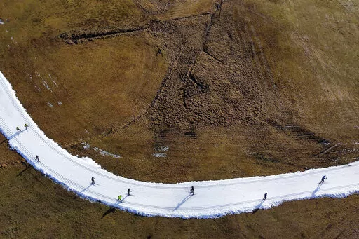 People ski on a cross country slope in Ramsau, Austria, Friday, Jan. 6, 2023. Sparse snowfall and unseasonably warm weather in much of Europe is allowing green grass to blanket many mountaintops across the region where snow might normally be. (AP Photo/Matthias Schrader, File)