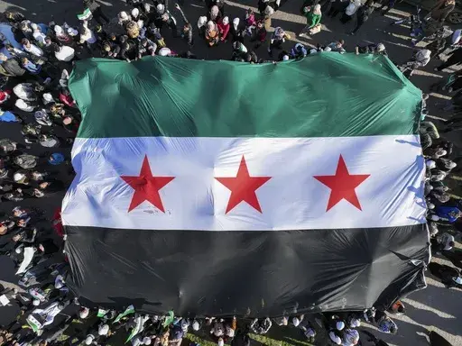 Syrians display a giant Syrian "revolutionary" flag during a celebratory demonstration following the first Friday prayers since Bashar Assad's ouster, in Damascus' central square, Syria, Friday, Dec. 13, 2024. (AP Photo/Ghaith Alsayed)