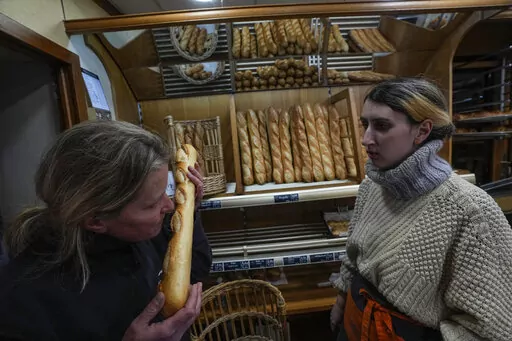 Bakery owner Florence Poirier, LEFT, smells the fresh baguette who comes out of the oven as Mylene Poirier stands next to her at a bakery, in Versailles, west of Paris, Tuesday, Nov. 29, 2022. The humble baguette -- the crunchy ambassador for French baking around the world -- is being added to the U.N.'s list of intangible cultural heritage as a cherished tradition to be preserved by humanity. UNESCO experts gathering Wednesday Nov. 30, 2022 in Morocco decided that the simple French flute deserv