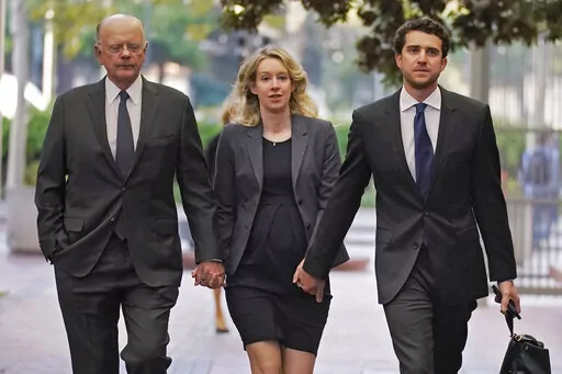 Former Theranos CEO Elizabeth Holmes, center, arrives at federal court with her father, Christian Holmes IV, left, and partner, Billy Evans, in San Jose, Calif., Monday, Oct. 17, 2022. In a motion filed Thursday, Jan. 19, 2023, in federal court in Northern California, federal prosecutors say Elizabeth Holmes is a flight risk and shouldn’t be allowed to stay out of prison while she appeals her 11-year prison sentence for defrauding investors. (AP Photo/Jeff Chiu, File)