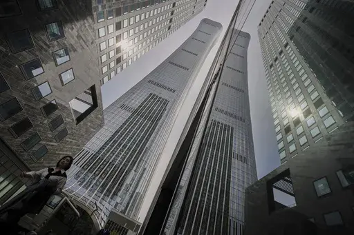 A woman walks by high rise office buildings in the central business district, in Beijing, Tuesday, April 8, 2025. (AP Photo/Andy Wong)