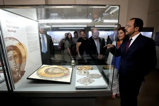 Cyprus' President Nikos Christodoulides, right, stands in front of an Orthodox Christian icon after the same was repatriated and displayed at the Archeological museum in capital Nicosia, Cyprus, Monday, July 22, 2024. The returned artifacts numbering around 60, including jewelry from the Chalcolithic Period dating between 3500-1500 BC, Bronze Age bird-shaped idols, jars and spearheads as well as many Orthodox Christian icons were part of a larger haul of 250 antiquities that German authorities h