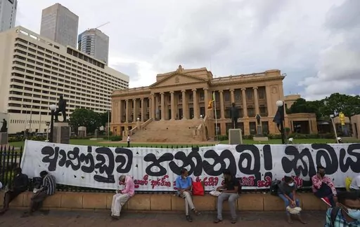 Sri Lankans sit by the fence of the president's office during an on going protest demanding president Gotabaya Rajapaksa resign, in Colombo, Sri Lanka, Friday, April 29, 2022. Gotabaya has agreed to replace his older brother as prime minister in a proposed interim government to solve a political impasse caused by the country's worst economic crisis in decades, a prominent lawmaker said Friday.Banner reads "Oust the government , Change the system." (AP Photo/Eranga Jayawardena)