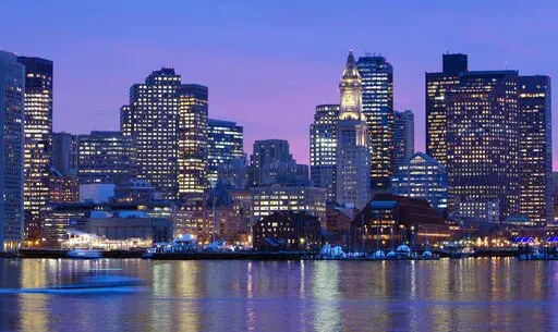 The Boston skyline is illuminated and reflected in the waters of Boston Harbor, on Jan. 6, 2012. On Tuesday, Sept. 13, 2022, the city joined the ranks of other major cities challenging their 2020 census figures, claiming the once-a-decade U.S. head count which determines political power and federal funding missed university students, the foreign-born and inmates at correctional facilities. (AP Photo/Michael Dwyer, File)