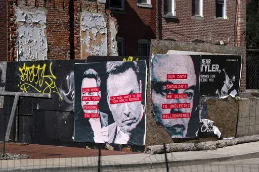 Posters showing the face of Elon Musk and messages relating to data privacy are seen on a fence surrounding a building site in Washington, Friday, March 7, 2025. (AP Photo/Ben Curtis)