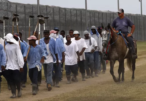 In this Aug. 18, 2011 photo, a prison guard rides a horse alongside prisoners as they return from farm work detail at the Louisiana State Penitentiary in Angola, La. After the Civil War, the 13th Amendment's exception clause, that allows for prison labor, provided legal cover to round up thousands of mostly young Black men. They then were leased out by states to plantations like Angola and some of the country's biggest privately owned companies, including coal mines and railroads. (AP Photo/Gera